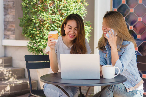Asiatiche giovani donne che lavorano su laptop utilizzando e cercando smartphone e bere caffè mentre seduto in caffè. Stile di vita donne comunicazione e lavoro nel concetto di caffetteria
. - Foto, immagini