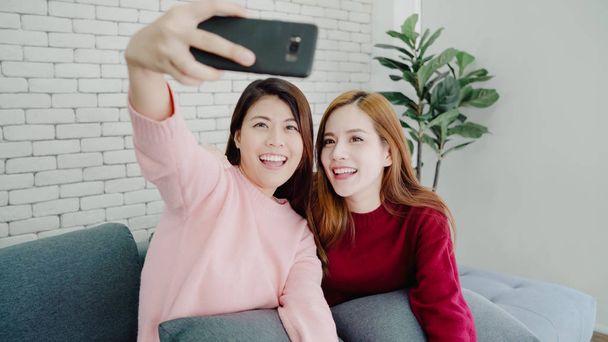Lesbisches asiatisches Paar mit Smartphone-Selfie im heimischen Wohnzimmer, süßes Paar genießt lustige Momente, während es zu Hause entspannt auf dem Sofa liegt. Lifestyle-Paar entspannt sich zu Hause. - Foto, Bild