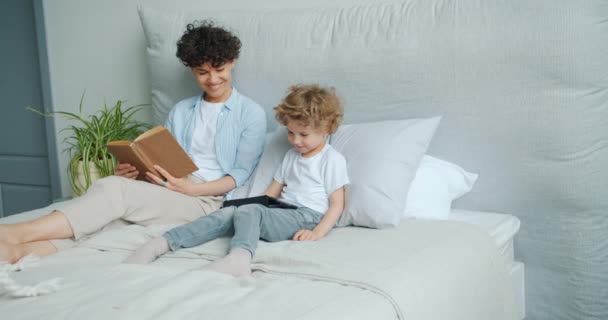 Young woman and small boy using tablet in bed smiling enjoying gadget together - Video, Çekim