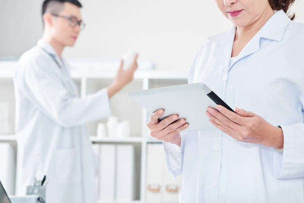 Médico maduro grave em testes de labcoat branco verificando os resultados do paciente no computador tablet
 - Foto, Imagem