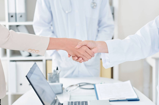 Doctor shaking hand of female patient over office table with opened laptop, selective focus - Foto, Bild