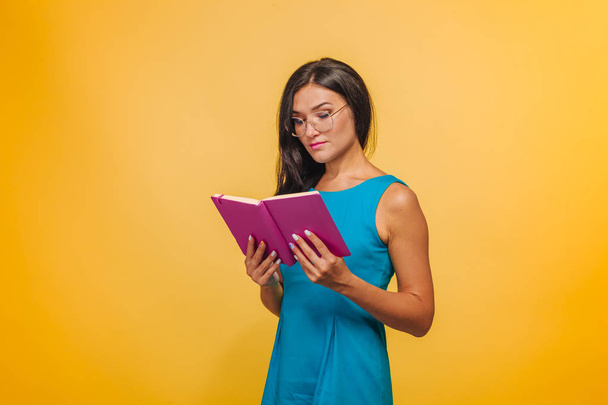Chica con gafas sobre un fondo amarillo en un vestido azul de lectura
 - Foto, Imagen