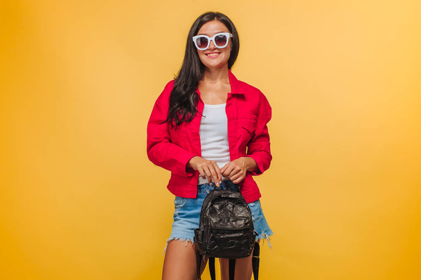 Girl on yellow background in red jacket with backpack - Fotó, kép