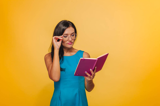 Mavi bir elbise okuma sarı bir arka plan üzerinde gözlüklü kız - Fotoğraf, Görsel