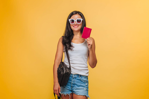 Bir sırt çantası ve bir passpo ile sarı bir arka plan üzerinde Kız turist - Fotoğraf, Görsel