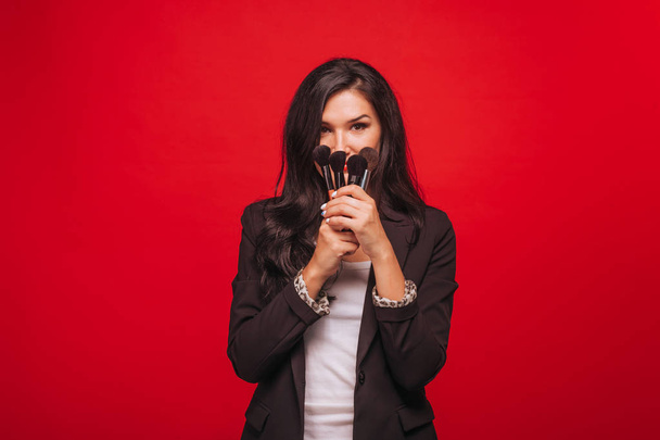 Девушка с кисточками для макияжа на красном фоне
 - Фото, изображение