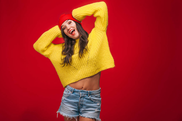 girl in a yellow sweater and a hat on a red background holding h - 写真・画像