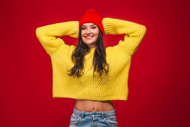 girl in a yellow sweater and a hat on a red background holding h - Φωτογραφία, εικόνα