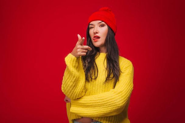 Κορίτσι με κίτρινο πουλόβερ και καπέλο σε κόκκινο φόντο δείχνει δάχτυλα u - Φωτογραφία, εικόνα