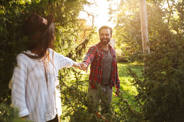 Изображение улыбающейся пары мужчины и женщины, держащих свои руки вместе, глядя друг на друга в зеленом парке
 - Фото, изображение