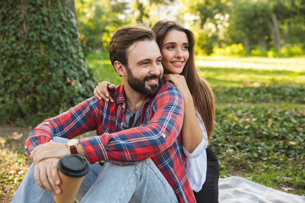 Imagen de pareja romántica hombre y mujer abrazando y bebiendo café para llevar mientras descansan en el parque verde
 - Foto, Imagen