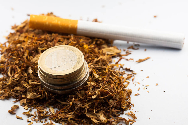 Shredded tobacco with euro coins around, isolated on white background. Tobacco can cause diseases in the organism. - Photo, Image