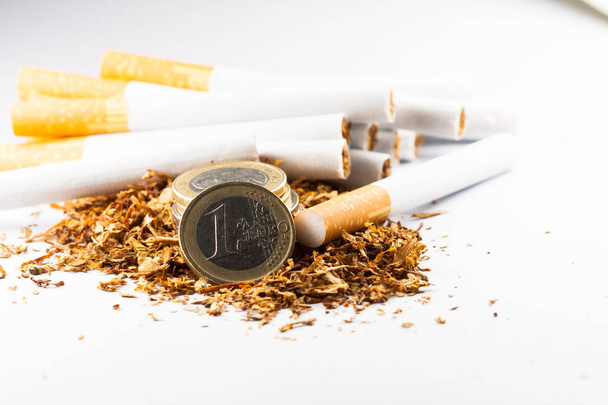 Shredded tobacco with euro coins around, isolated on white background. Tobacco can cause diseases in the organism. - Photo, Image