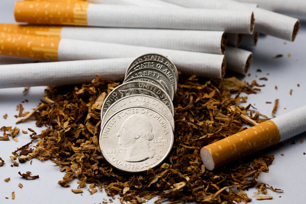 Cigarettes separated with some shredded tobacco scattered, with coins in pennies around, isolated on white background. Tobacco can cause diseases in the organism. - Photo, Image