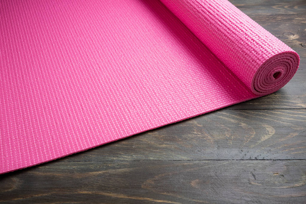 Ροζ χαλάκι γιόγκα σε ξύλινο φόντο. Εξοπλισμός για γιόγκα. Έννοια  - Φωτογραφία, εικόνα