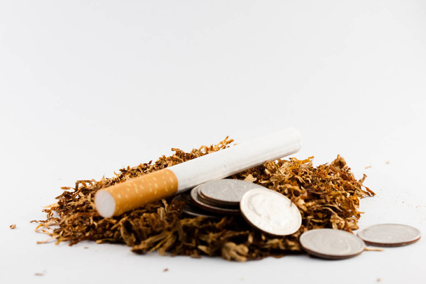 Cigaretta elválasztott néhány felaprított dohány szétszórva, az érmék fillérekért körül, elszigetelt fehér háttér. A dohány betegségeket okozhat a szervezetben. - Fotó, kép
