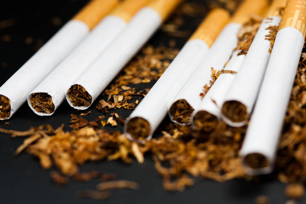 Papierosy na ilości rozdrobnionych tytoniu odizolowanych na czarnym tle. Tytoń może powodować choroby. - Zdjęcie, obraz