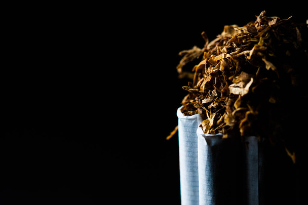 De nombreuses cigarettes de tabac isolées sur fond noir avec du tabac déchiqueté dessus. Le tabac peut causer des maladies
. - Photo, image