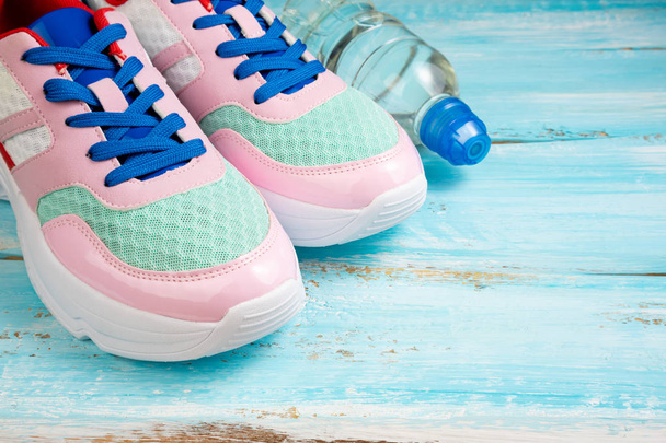 Pembe spor ayakkabı ve mavi ahşap arka plan üzerinde su şişesi.  - Fotoğraf, Görsel
