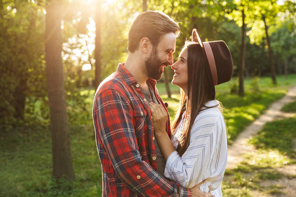 Cheerful pleased romantic young loving couple walking outdoors in a green nature park forest kissing. - 写真・画像