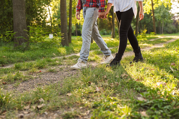 Bijgesneden foto van een jonge liefdevolle paar wandelen buiten in een groene natuurpark bos. - Foto, afbeelding