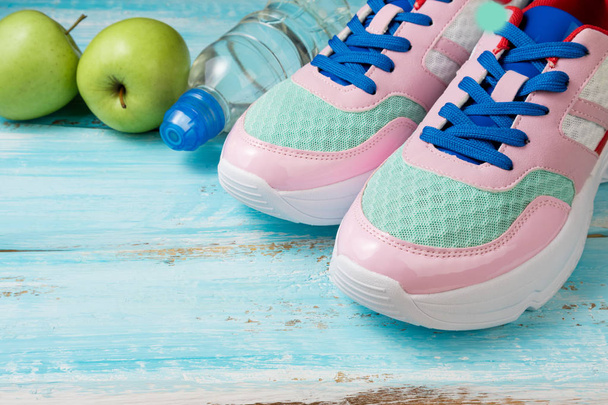 Scarpe sportive rosa, bottiglia d'acqua e mele verdi su legno blu
 - Foto, immagini
