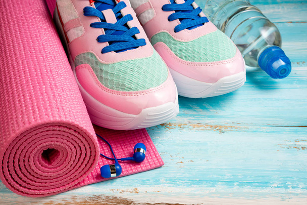 Розовый коврик для йоги, спортивная обувь, бутылка воды и наушники на блюе
 - Фото, изображение