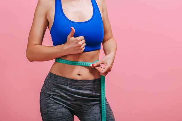 skinny girl measures waist and shows thumb on pink background - Photo, Image