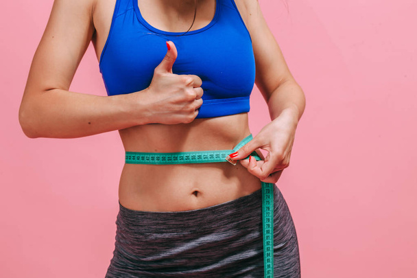 skinny girl measures waist and shows thumb on pink background - Foto, Imagem