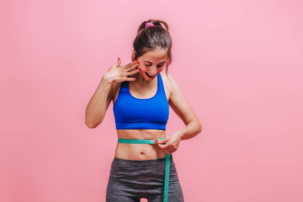girl measures a waist on a pink background - Φωτογραφία, εικόνα
