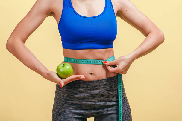 Mädchen misst Taille und zeigt grünen Apfel auf gelbem Hintergrund - Foto, Bild