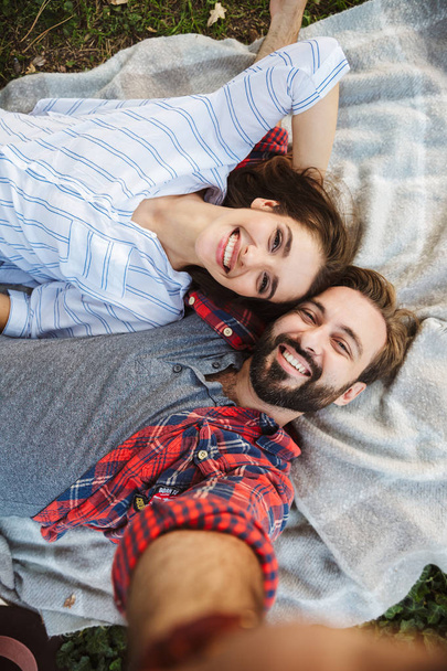 Image of laughing couple man and woman taking selfie photo while lying in green park - Photo, Image