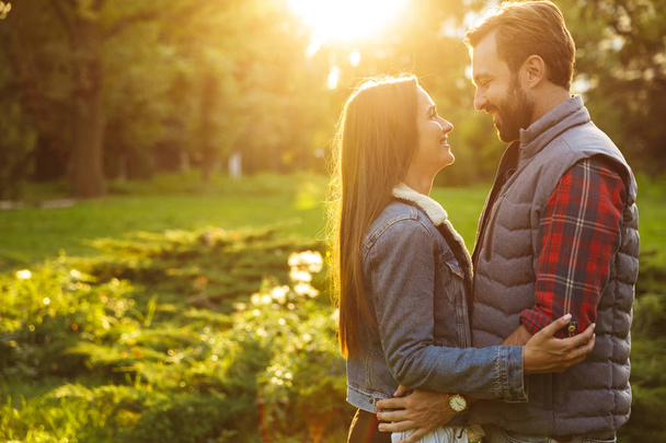 Зображення щасливої пари чоловік і жінка обіймаються і дивляться один на одного під час прогулянки в зеленому парку
 - Фото, зображення
