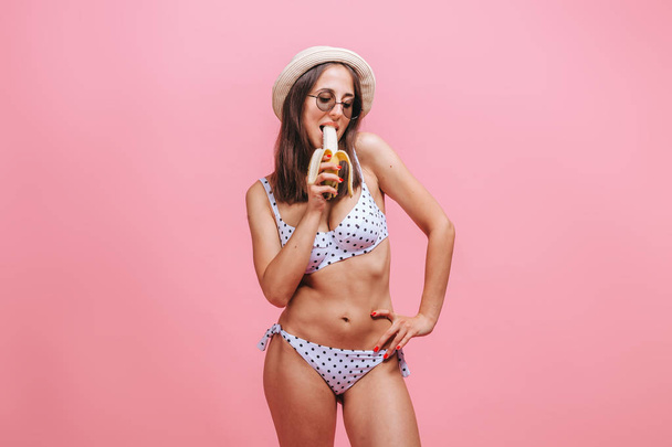The girl eats a banana in a swimsuit, hat and sunglasses on a pi - Foto, Imagem