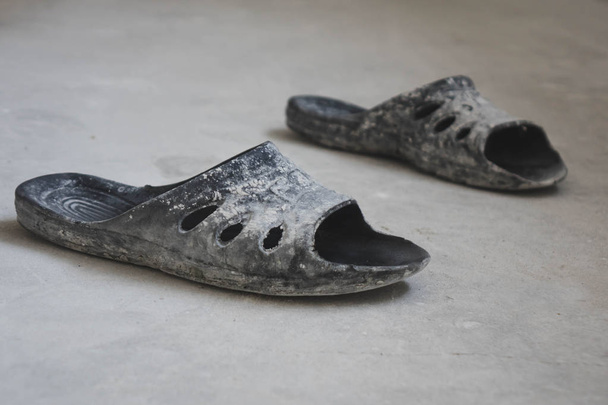 black rubber flip-flops standing on a concrete floor, the concept of repair. - Photo, Image