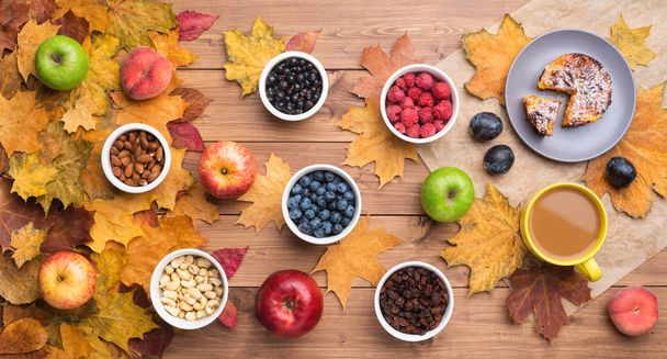 Seasonal autumn background. Frame of colorful maple leaves and a cake, berries, raisins, apples, fruits, coffee and nuts over wooden background. - Фото, зображення