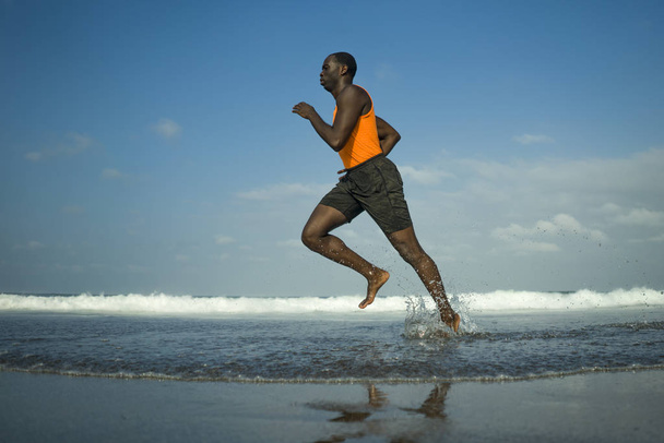 athletic full body portrait of young attractive and fit black afro American man running on the beach doing Summer fitness jogging workout at the sea in healthy lifestyle concept  - Zdjęcie, obraz