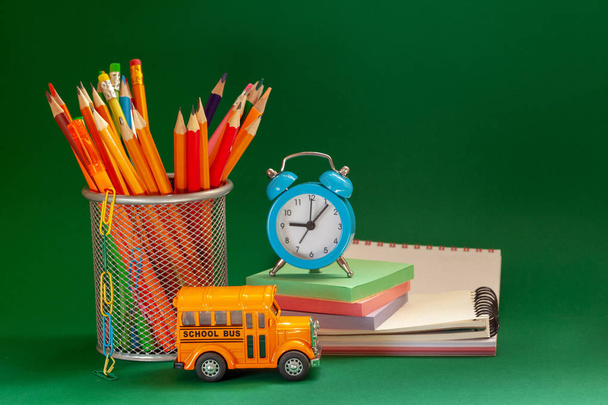 Education and back to school concept. Yellow retro school bus and pencils in basket, textbooks and alarm clock on dark green background. - Fotografie, Obrázek