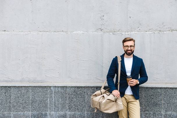 Portrait of bearded businessman wearing eyeglasses holding paper cup and carrying bag - Valokuva, kuva