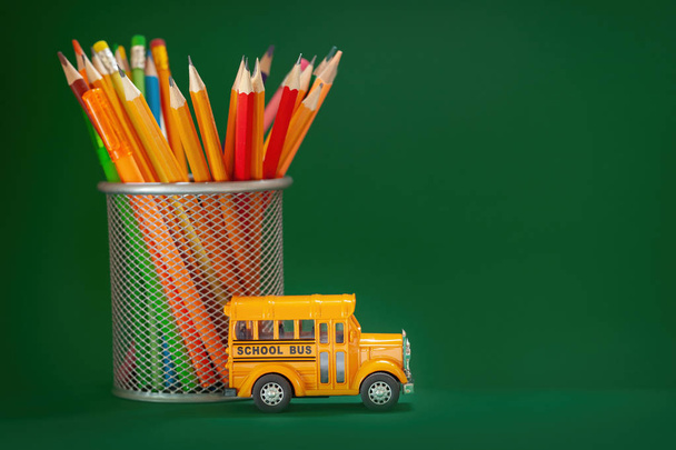 Education and back to school concept. Yellow retro school bus and pencils in basket on dark green background. - Foto, Imagem