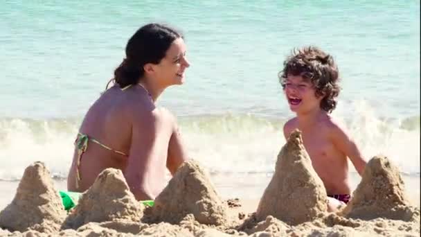 Irmã mais velha brincando com o irmão mais novo na praia de areia durante o dia
  - Filmagem, Vídeo