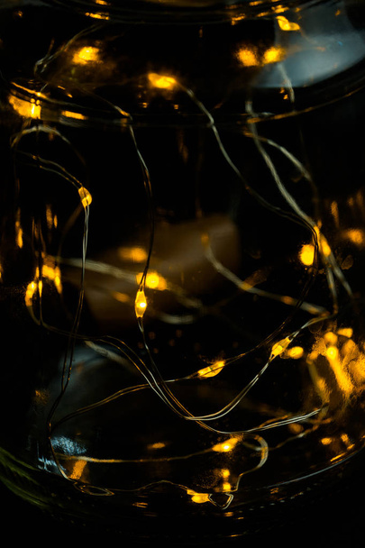 Decorative lights in glass jar at the dark room with mirror effect on dark background. Festive decorations .Warm white led lights. - Foto, imagen
