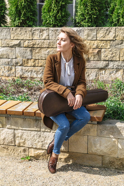 Young woman with violin sitting on wooden bench - Foto, imagen