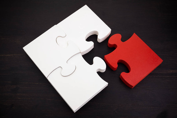 Three onnected jigsaw puzzle pieces and one red on dark wooden background. Finding the right solutions in teamwork. - Foto, Imagem
