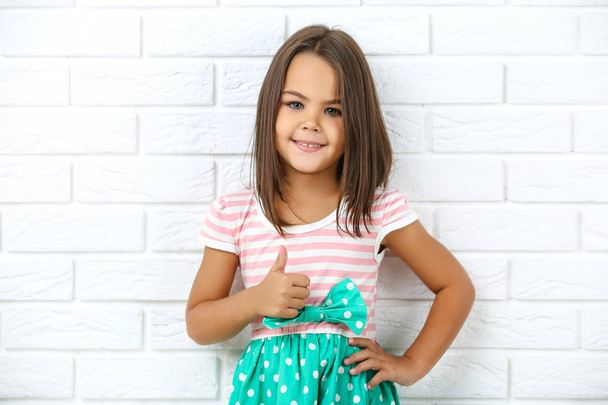 Beautiful little girl showing thumb up on white brick wall backg - Foto, Bild