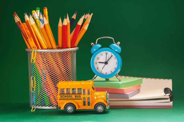 Education and back to school concept. Yellow retro school bus and pencils in basket, textbooks and alarm clock on dark green background. - Valokuva, kuva