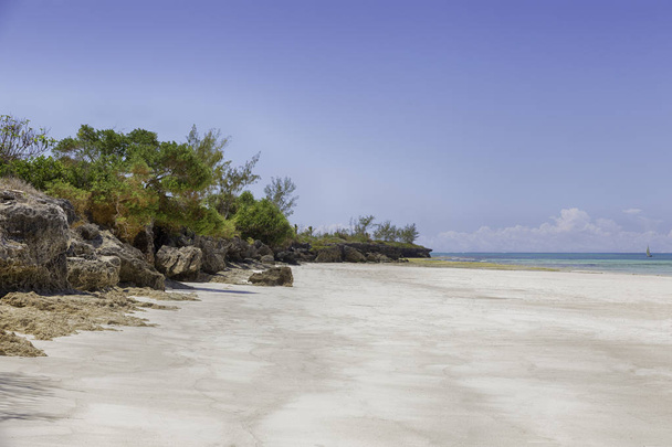 Playa de arena tropical blanca con acantilado rocoso bajo el cielo azul
 - Foto, Imagen