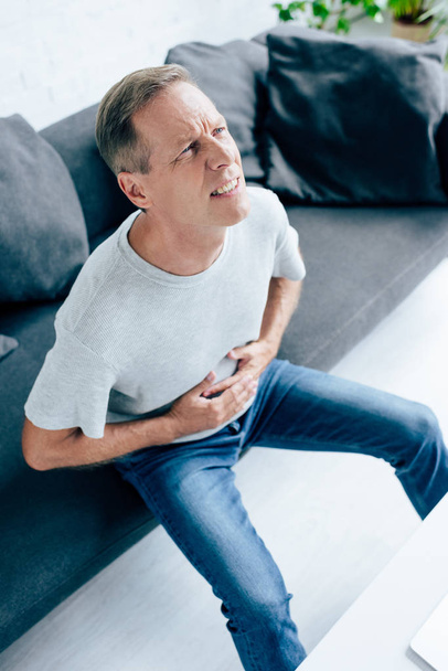 high angle view of handsome man in t-shirt with stomachache  - Fotografie, Obrázek