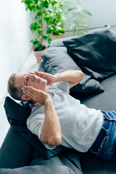 handsome man in t-shirt with closed eyes touching head in apartment  - Photo, image