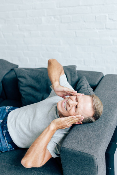high angle view of handsome man in t-shirt with closed eyes touching head in apartment  - Foto, immagini